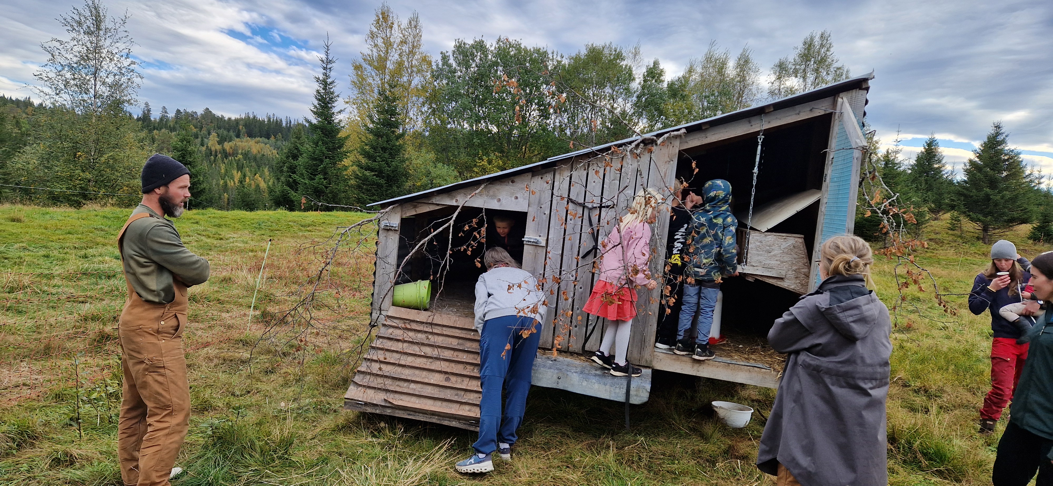 Folk som samles rundt eldre bygning i naturlandskap